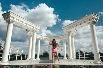 the girl stands with her back to the camera against the backdrop of a white colonnade with...