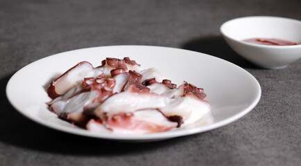 Thinly sliced octopus and red pepper paste on a white plate. Fresh seafood dishes.
