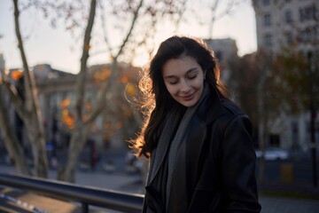 A woman wearing a black jacket and scarf is smiling at the camera