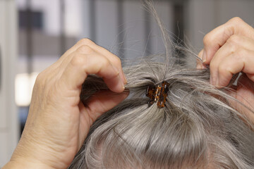 white-haired woman making a ponytail with a hair clip