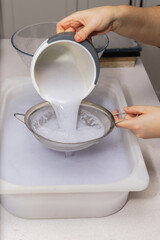 closeup of a woman's hands straining recycled paper pulp with a strainer