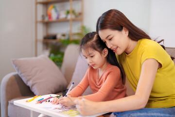 A mother assisting her daughter with homework at the table, surrounded by books and stationery,...