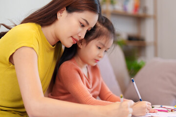 Fototapeta premium A mother assisting her daughter with homework at the table, surrounded by books and stationery, fostering learning and support.