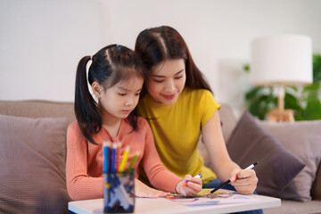A mother assisting her daughter with homework at the table, surrounded by books and stationery,...