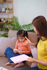 A mother scolding her daughter for excessive phone usage while sitting together on the sofa, focusing on discipline and balance.