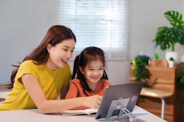 A mother is teaching her young daughter to do homework together at the table, creating a supportive and educational environment.