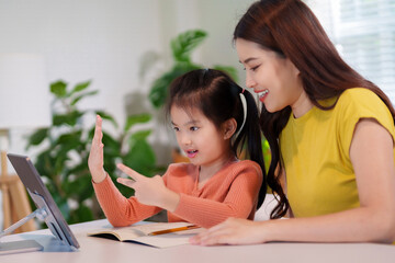 A mother is teaching her young daughter to do homework together at the table, creating a supportive and educational environment.