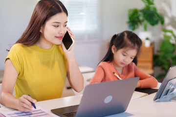 A mother and her daughter are working on homework together at the table, using a laptop for research.