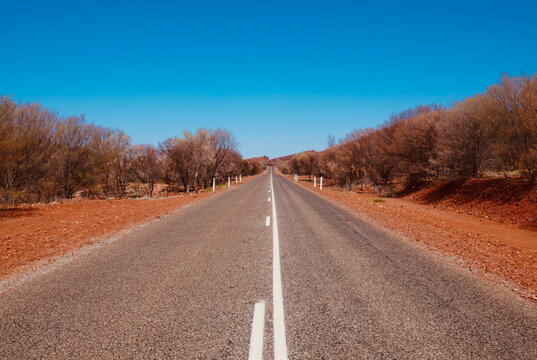Scenic road in the remote Australian outback with red dirt and bushland, Northern Territory