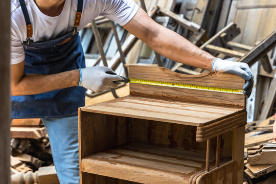 Male carpenter measuring wood furniture in carpentry workshop