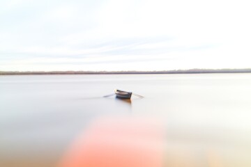Lonely boat gliding across tranquil water, surrounded by soft, m