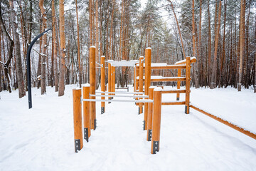 A charming wooden playground is entirely blanketed in soft, fluffy white snow, creating a truly picturesque winter wonderland scene in the beautifully serene surrounding woods nearby