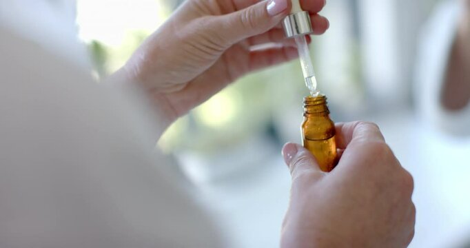 Using dropper to add liquid into bottle, mature woman preparing essential oils