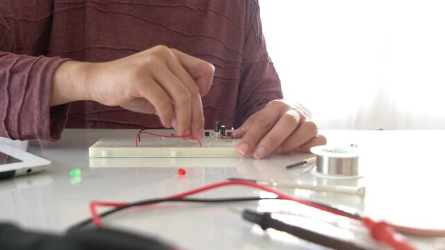 A person working on an electronics project, assembling a circuit board with wires and components. The focus is on hands interacting with the board, highlighting the process of learning and experimenta
