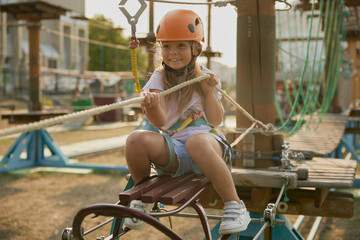 Playful little girl child pulling hawser while overcoming obstacles at rope park