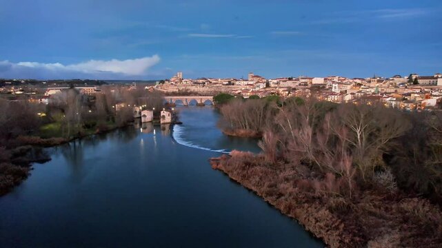 Aerial traveling along the Duero River, passing by the water mills and showing the stone bridge and the cathedral, Zamora, Spain