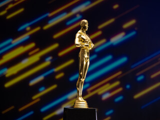 A golden Oscar statue stands on a black base in front of a colorful background
