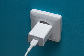 White phone charger is plugged into a white socket on a cyan-painted wall.