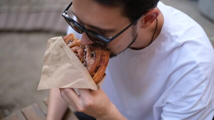 young European man eating sweet pastries on the summer terrace of a cafe on a hot summer day