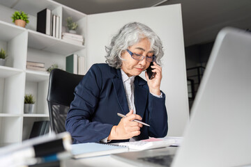 Elderly business woman managing tasks while on the phone in a modern office setting