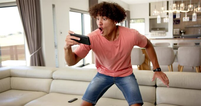 Surprised man holding smartphone and reacting to shocking news at home