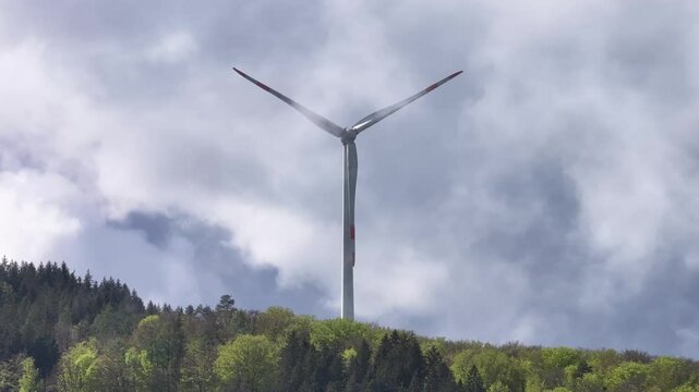 Ein Windrad dreht sich langsam vor blauem Himmel. Um das Winrad herum wandern wei&szlig;e Wolken und Nebel an einem sch&ouml;nen Sonnenaufgang. Die Sonne zeigt sich durch den vor kurzem verschwundenen Regen