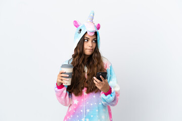 Young caucasian woman wearing a unicorn pajama isolated on white background holding coffee to take away and a mobile while thinking something © luismolinero