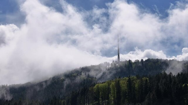 Ein Windrad dreht sich langsam vor blauem Himmel. Um das Winrad herum wandern wei&szlig;e Wolken und Nebel an einem sch&ouml;nen Sonnenaufgang. Die Sonne zeigt sich durch den vor kurzem verschwundenen Regen