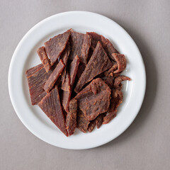 Sweet and spicy beef jerky on a white plate, showcasing a delicious snack option for meat lovers