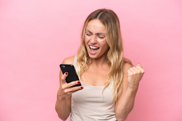 Young Russian woman isolated on pink background using mobile phone and doing victory gesture