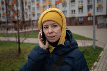 Woman talking on the phone on the street, person walking in an urban area, holding a mobile device for communication.