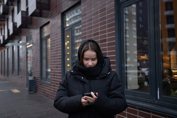 Fototapeta premium Teenage girl with phone on city street, teenager enjoying technology outside, typing messages while walking in an urban area.