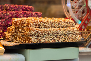 Close-up of Turkish delight bars covered in chopped nuts, displayed alongside colorful varieties in a confectionery shop.