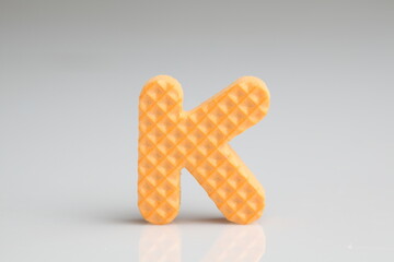 k alphabet in orange color foam on a white background
