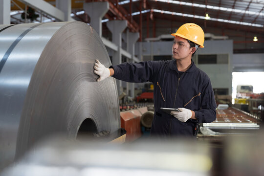 Metalwork manufacturing, warehouse of raw materials. Asian male factory worker inspecting quality rolls of galvanized or metal sheet. Male worker working in warehouse of raw materials
