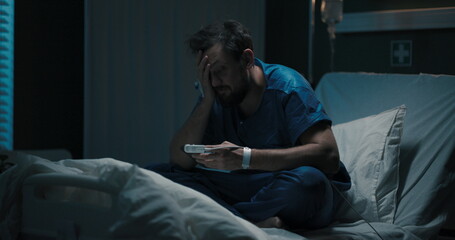 Patient sits on hospital bed, scrolling through phon.