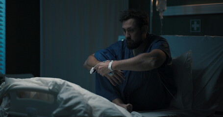 Fototapeta premium Patient sits, holding head, swaying on bed.