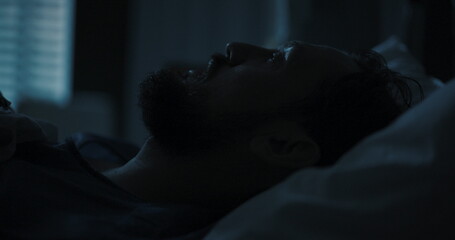 Young man lays in a hospital bed, his gaze fixed on the ceiling, lost in thought.