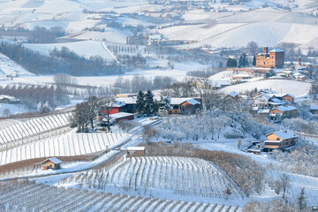 Winter countryside scene with snow-covered vineyards on the hills and a small village in Italy.