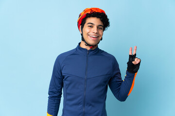 Venezuelan cyclist man isolated on blue background smiling and showing victory sign