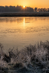 Beautiful atmospheric Winter sunrise landscape image of frozen fields and grasses with sun glow on the frosty ground