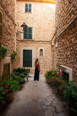 A quiet cobblestone street in Fornalutx, Mallorca, surrounded by stone buildings adorned with lush greenery and traditional wooden shutters. A moment of authentic Mallorcan charm for travelers