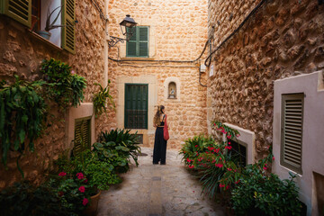 A charming alley in Fornalutx, Mallorca, featuring rustic stone walls, lush plants, and a traveler enjoying the quiet ambiance of this historic Mediterranean village.