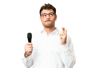 Brazilian man picking up a microphone over isolated chroma key background with fingers crossing and wishing the best