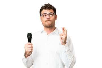 Brazilian man picking up a microphone over isolated chroma key background with fingers crossing and wishing the best