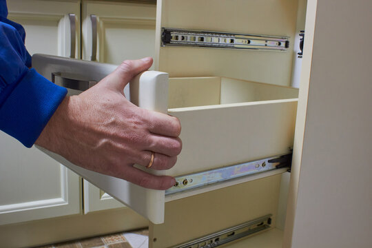 carpenter hands installing drawer on sliding skids,Close up of hands installing wooden drawer on sliding skids in contemporary cupboard cabinet