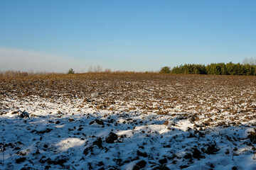A plowed agricultural field to the horizon is lightly covered with snow.