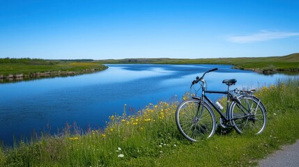 Fototapeta premium A bicycle parked beside a winding river under a bright blue sky.