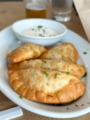 Top view of crispy empanadas served with a creamy dipping sauce and garnished with chopped herbs.