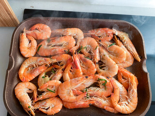 Shrimp cooking in a skillet, garnished with herbs, releasing steam